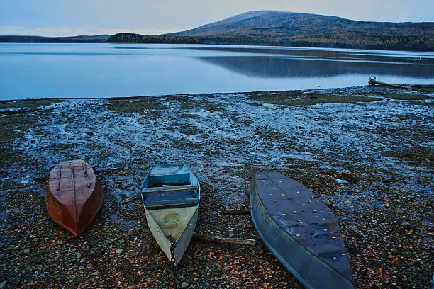 Boats lie on the stony shore of the pond with mountains in the background