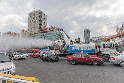 Urumqi, Xinjiang, China - October 4, 2016: Water fog spray truck work on the street and try to decrease the dust in the air.Office building on the background, and incidental people on the street.