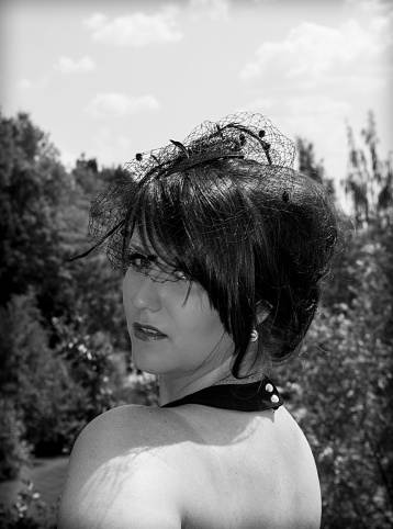 Black and white portrait of an attractive woman wearing a halter neck top turning to look over her shoulder at the camera outdoors in the garden