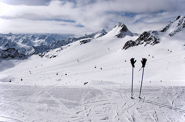 Ski poles, gloves and slopes on Tiefenbach glacier in Solden Ski poles with ski gloves, gondola cable car, ski tow, and skiers on the slope on Tiefenbach glacier in Solden ski resort in Otztal Alps, Tirol, Austria tiefenbach stock pictures, royalty-free photos & images