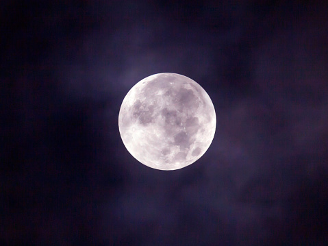 Full moon rising among the clouds at dusk