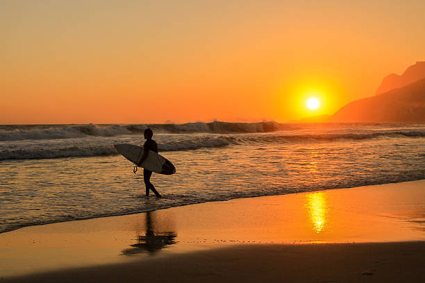 Rio de Janeiro, Brazil - October 31, 2016: Surfer going to the Ipanema sea, in Brazil, on the sunset, with reflex on the sand