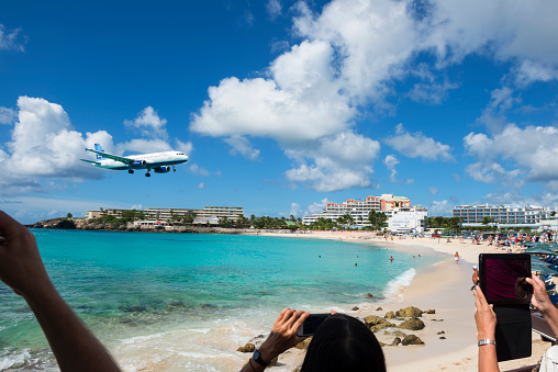 Maho Beach, St. Maarten - November 15, 2013: People at Maho Beach watch a JetBlue Airbus A320 come in for a landing at Princess Juliana International Airport in St. Maarten. People are using smartphones and iPods to take photographs.