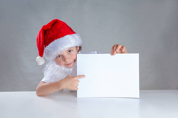 little santa peeping from behind white envelope and shows it - christmas child little boys peeking imagens e fotografias de stock