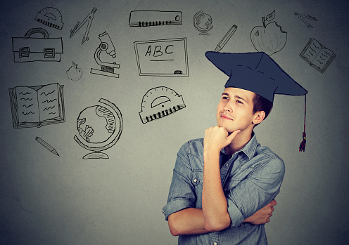 Young handsome man with graduation hat looking up thinking about education isolated on gray wall background