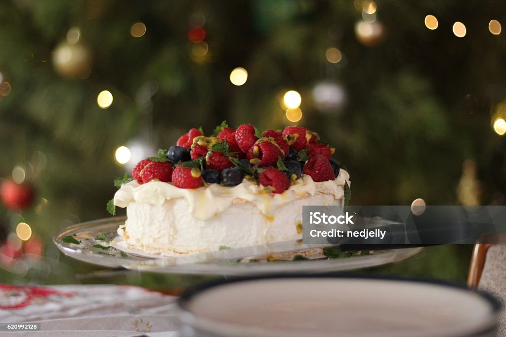 Pavlova with berries and passionfruit at Christmas time Delicious pavlova with cream, berries, passionfruit and mint. A staple of Australian Christmas lunch. Here it is in front if the Christmas tree where you can see defocussed Christmas lights and baubles. Christmas Stock Photo