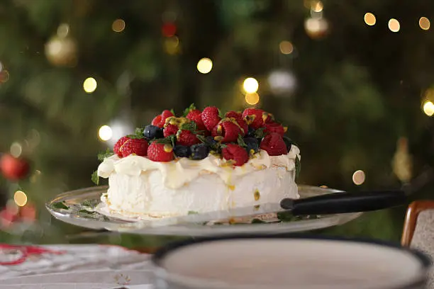 Delicious pavlova with cream, berries, passionfruit and mint. A staple of Australian Christmas lunch. Here it is in front if the Christmas tree where you can see defocussed Christmas lights and baubles.