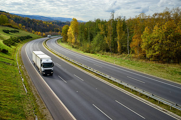 istock Asphalt expressway with oncoming white trucks in the autumn landscape. 620993388
