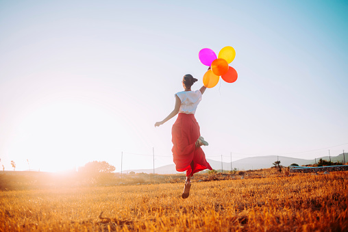 young woman joyfully jumping in the field holding colorful balloons,nice warm light and sunbeam