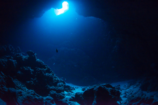 underwater landscape. cave in the coral reef lit sun rays.