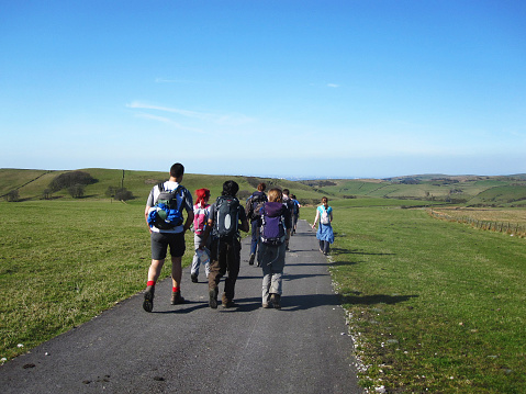 Peak District, United Kingdom - March 25, 2012: A group of young people hiking in the countryside of the Peak District National Park in northern England. Manchester city visible in the distance.