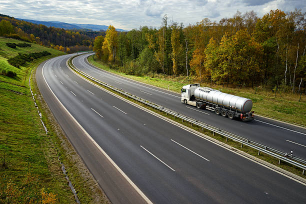 Expressway with driving a silver tanker in the autumn landscape.