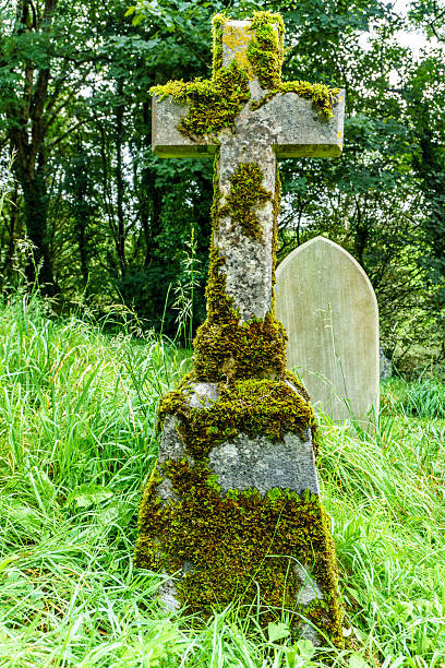 istock Stone graveside cross in cemetery covered in moss 621102562