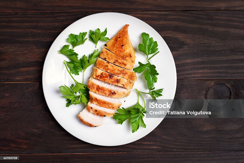 Roasted chicken breast Roasted chicken breast decorated with parsley on white plate over wooden background, top view Plate Stock Photo