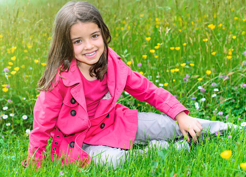 Summer portrait of happy cute child sitting in a grass of a flower garden