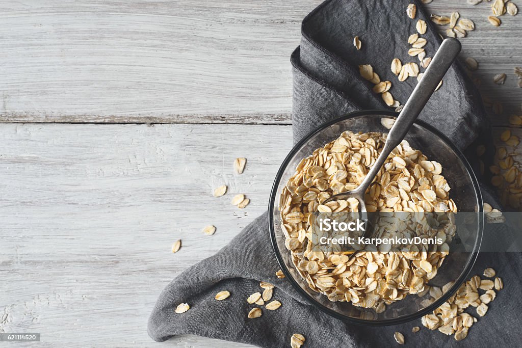 Oat flakes in a glass bowl on the wooden table Oat flakes in a glass bowl on a white wooden table Oatmeal Stock Photo