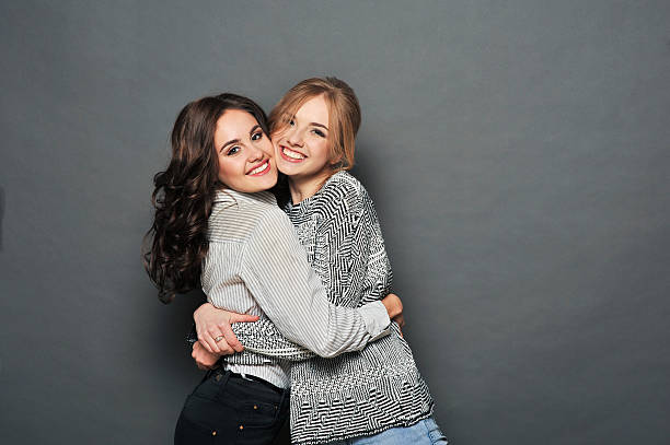young beautiful brunette and blond haired girls young beautiful brunette and blond haired girls hugs in front of gray background number 2 photos stock pictures, royalty-free photos & images