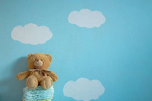 The toy is sitting on the diapers in the wall background of blue sky and clouds