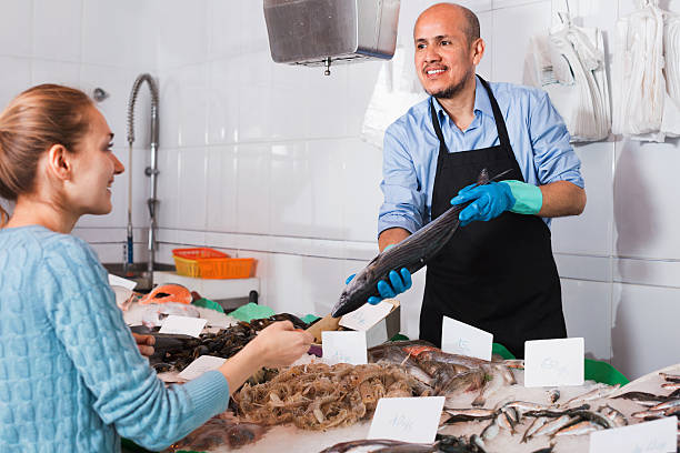 Pleasant seller helping female customer to choose  fish