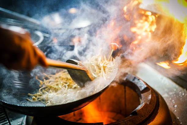 Chef in restaurant kitchen at stove with high burning flames