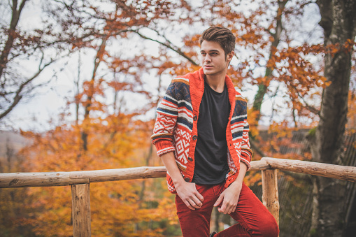 Young hipster standing on a bridge in the forest, enjoying the autumn.