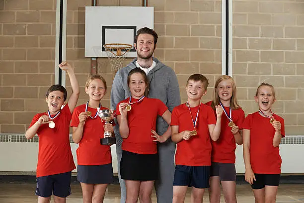 Photo of Victorious School Sports Team With Medals And Trophy In Gym