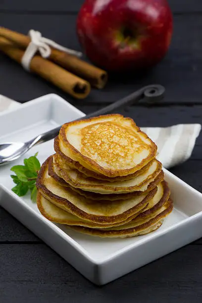 Homemade pancakes on the white rectangular plate on the black wooden table. Homemade pancakes in old fashion style. Rustic style spoon. Black background.