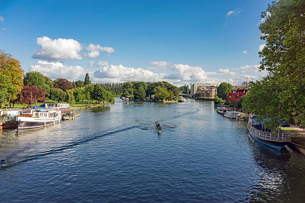 The River Thames at Reading in Berkshire, UK. Reading, UK - October 2nd 2016: Rowers navigate the River Thames at Reading in Berkshire. The large Christchurch Meadows park is to the left and Reading town centre is to the right. People can be seen in the distance enjoying the park on a sunny Autumnal day. thames river stock pictures, royalty-free photos & images