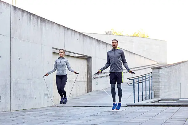 fitness, sport, people, exercising and lifestyle concept - man and woman skipping with jump rope outdoors