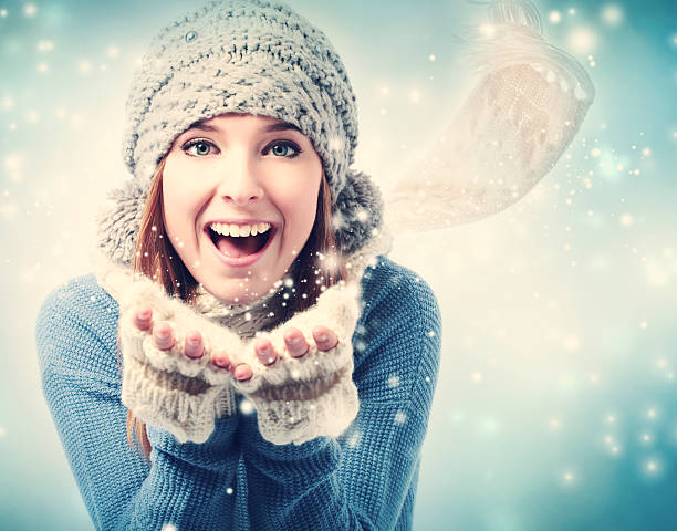 Happy young woman blowing snow in snowy day