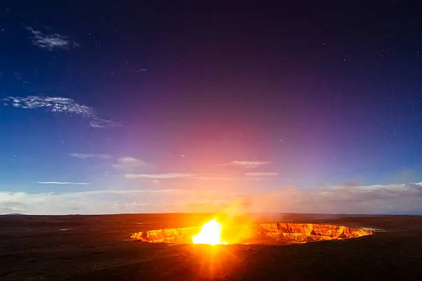 This is a horizontal, royalty free stock photograph of the Halema'uma'u Crater view from the Jaggar Museum Overlook and flames from the Kilauea volcano Caldera at night in Volcanoes National Park on the Big Island of Hawaii. Their are stars in the bright night sky background. Photographed with a Nikon D800 DSLR camera.