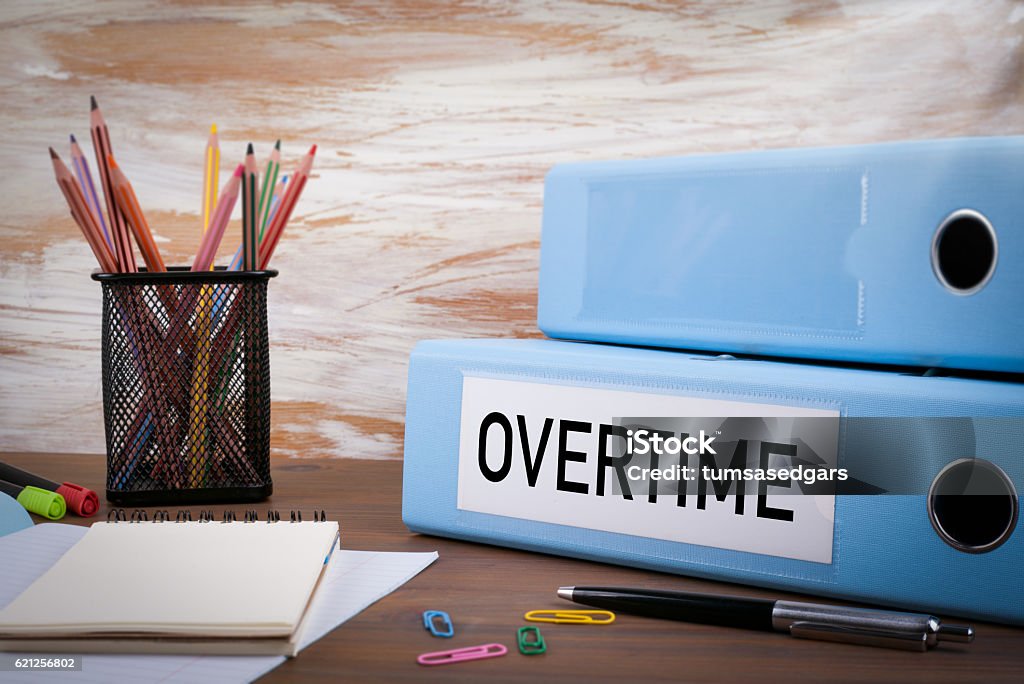 Overtime, Office Binder on Wooden Desk Overtime, Office Binder on Wooden Desk. On the table colored pencils, pen, notebook paper Working Late Stock Photo