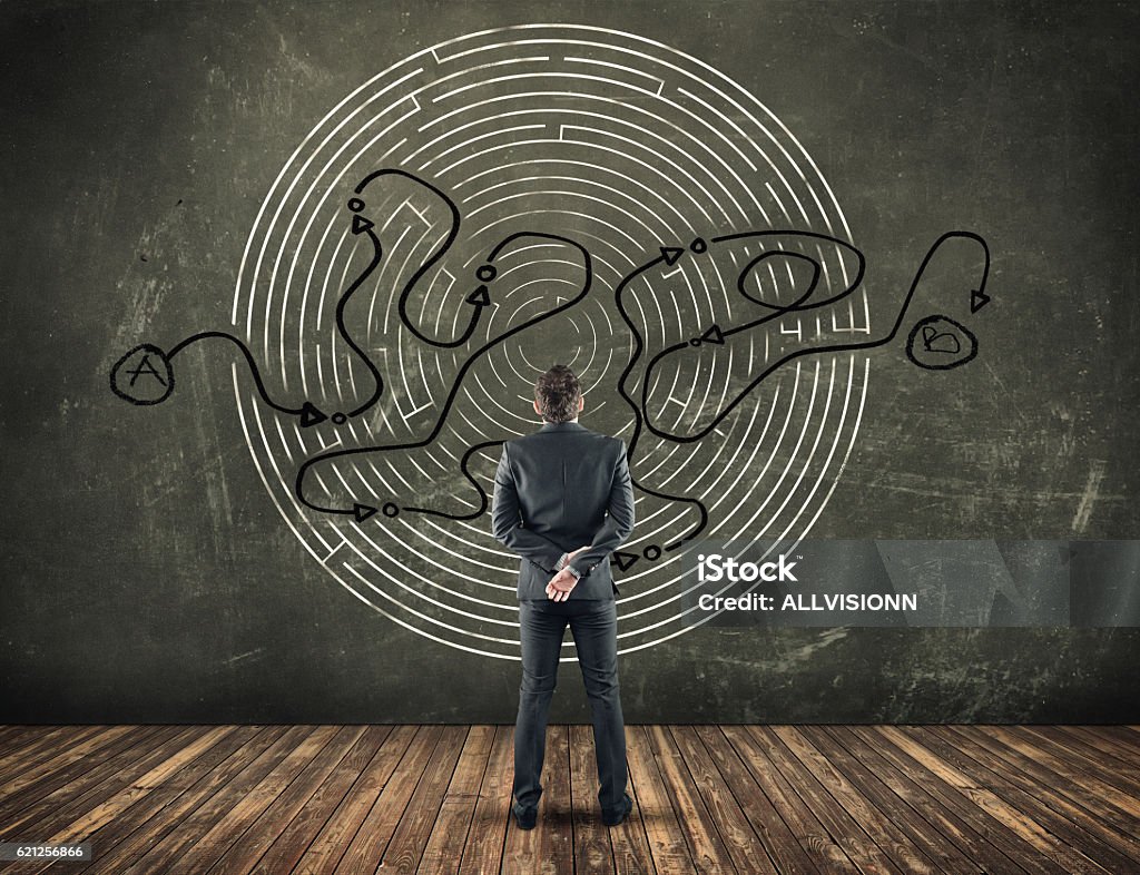 Business concept. Back view of businessman looking at a maze on a blackboard with a shorten path , from the point A to point B . Complexity Stock Photo