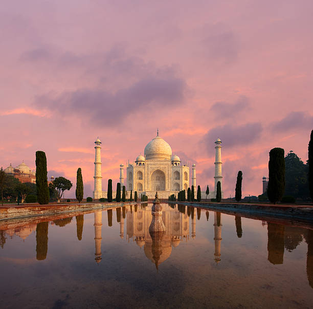 Nobody present as Taj Mahal glows beautifully at sunset reflected in front garden water fountain pool of water under a dramatic pink sky in Agra, Uttar Pradesh, India. Plenty of copy space
