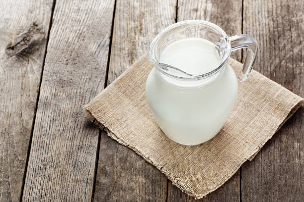 jarra de vidrio con leche sobre fondo de madera - botella de boca ancha fotografías e imágenes de stock