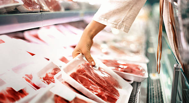 Buying meat at a supermarket. Closeup side view of unrecognizable woman chossing some fresh meat at local supermarket. The meat is cut into chops and packed into one pound packages. She has reached for a package of beef sirloin steaks. refrigerated section supermarket photos stock pictures, royalty-free photos & images