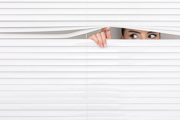 portrait of a woman looking through out the blinds. - peeking imagens e fotografias de stock