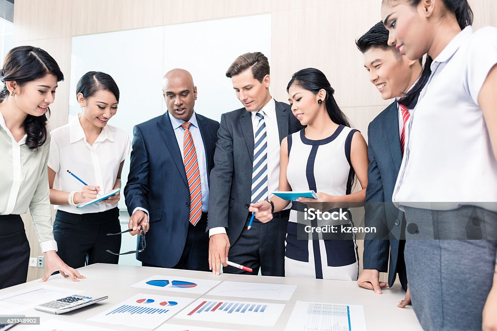 Business team discussing graphs and numbers in meeting Business team discussing graphs and numbers in meeting, men and women of Chinese, Caucasian, Indonesian, and Indian ethnicity Multiracial Group Stock Photo
