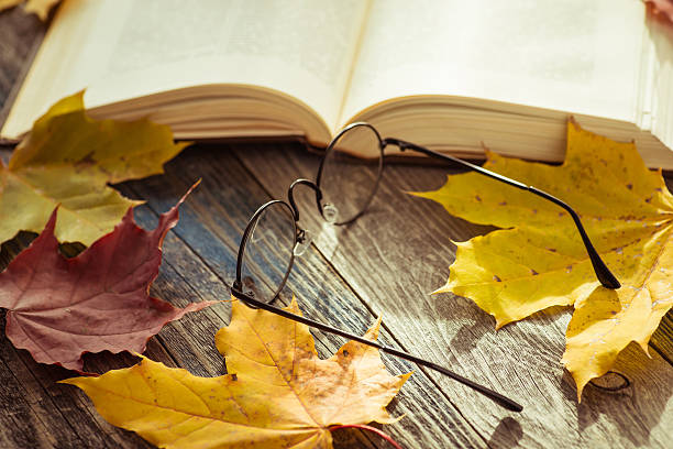 istock Eye glasses with book and autumn leaves on table 621353380
