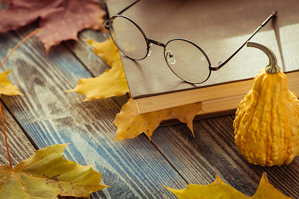 istock Eye glasses with book and autumn leaves on table 621353582