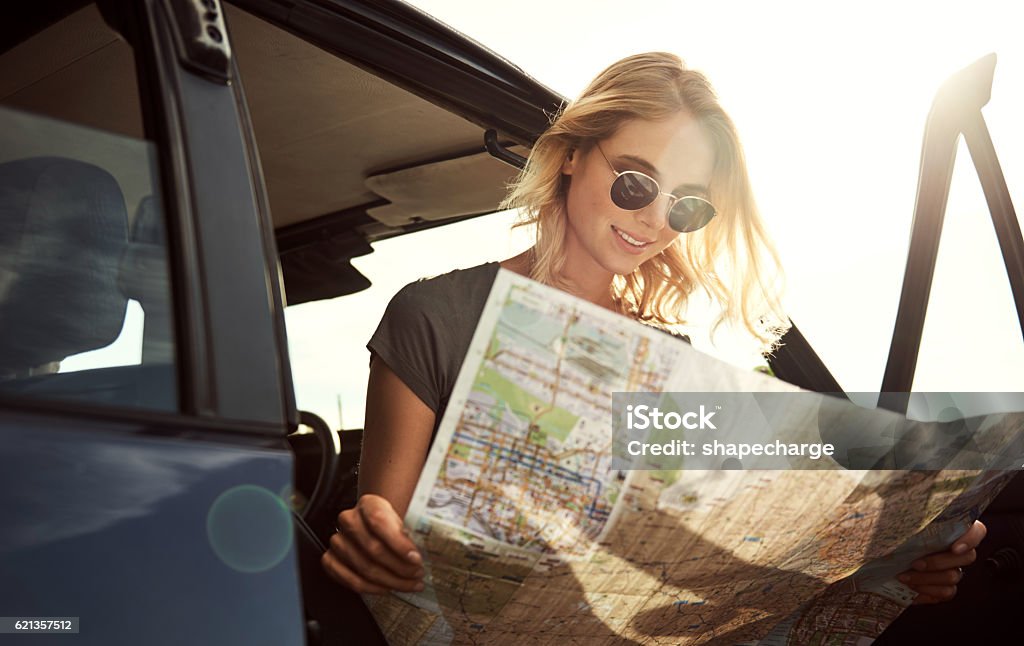 Always refer to the map Shot of an attractive young woman looking at a map while on a roadtrip Car Stock Photo