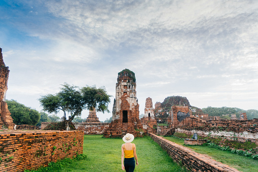 Young Caucasian woman walking near the ruins of ancient Buddhist Temple, Ayutthaya, Thailand