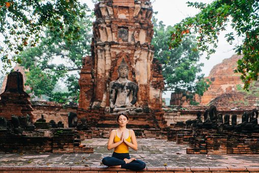 Young Caucasian woman doing yoga near the ruins of Buddhist Temple and statue of Buddha in Ayutthaya, Thailand