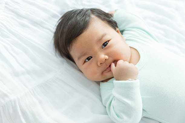 Adorable baby girl suck thumb on the bed Adorable baby girl suck thumb on the bed with copy space. This is growth development behavior. korean baby stock pictures, royalty-free photos & images
