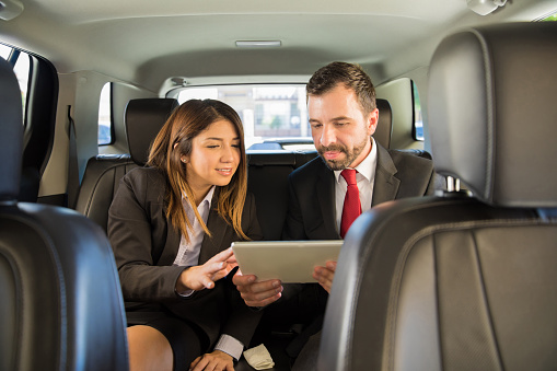 Attractive young businesspeople traveling by car and using a tablet computer for work