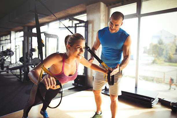 Woman doing arm exercises with suspension straps at gym.