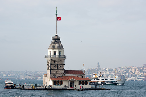 Istanbul, Turkey - November 6, 2016: Photo of Kız Kulesi (Maiden's Tower), vapur (passenger ferry of Istanbul) and Galata Tower are in the same photo. Galata Tower is in the background. Tourists are visiting Kız Kulesi, which is an island on the bosphorus. Turkish flag is waving at the top of Kız Kulesi.