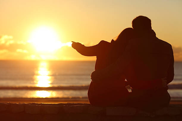 пара наслаждаясь закатом на пляже зимой - sun watch стоковые фото и изображения