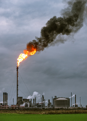 Dark smoke rising at dusk from a large flare flame at Grangemouth Petrochemical Plant in central Scotland.