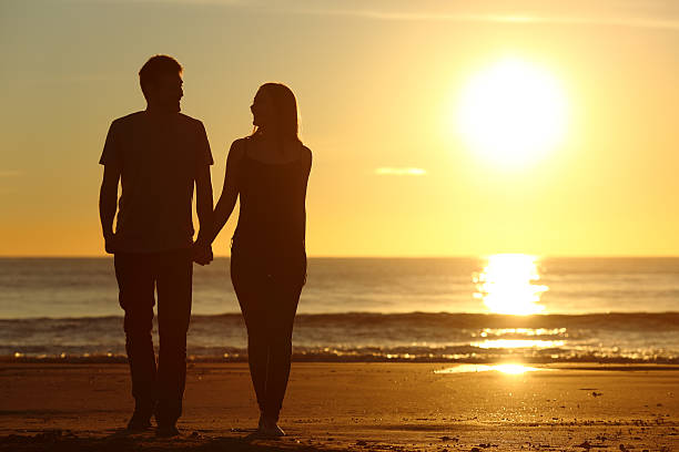 istock Couple silhouette walking together on the beach 621379778